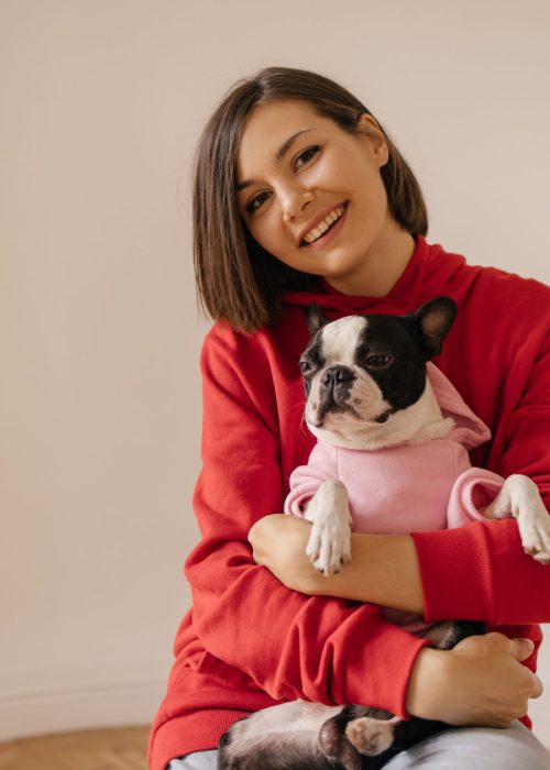 Beautiful caucasian young girl smiles at camera, gently holding dog on white background. Animal love concept