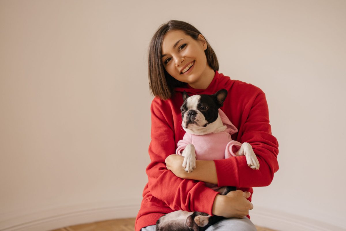 Beautiful caucasian young girl smiles at camera, gently holding dog on white background. Animal love concept